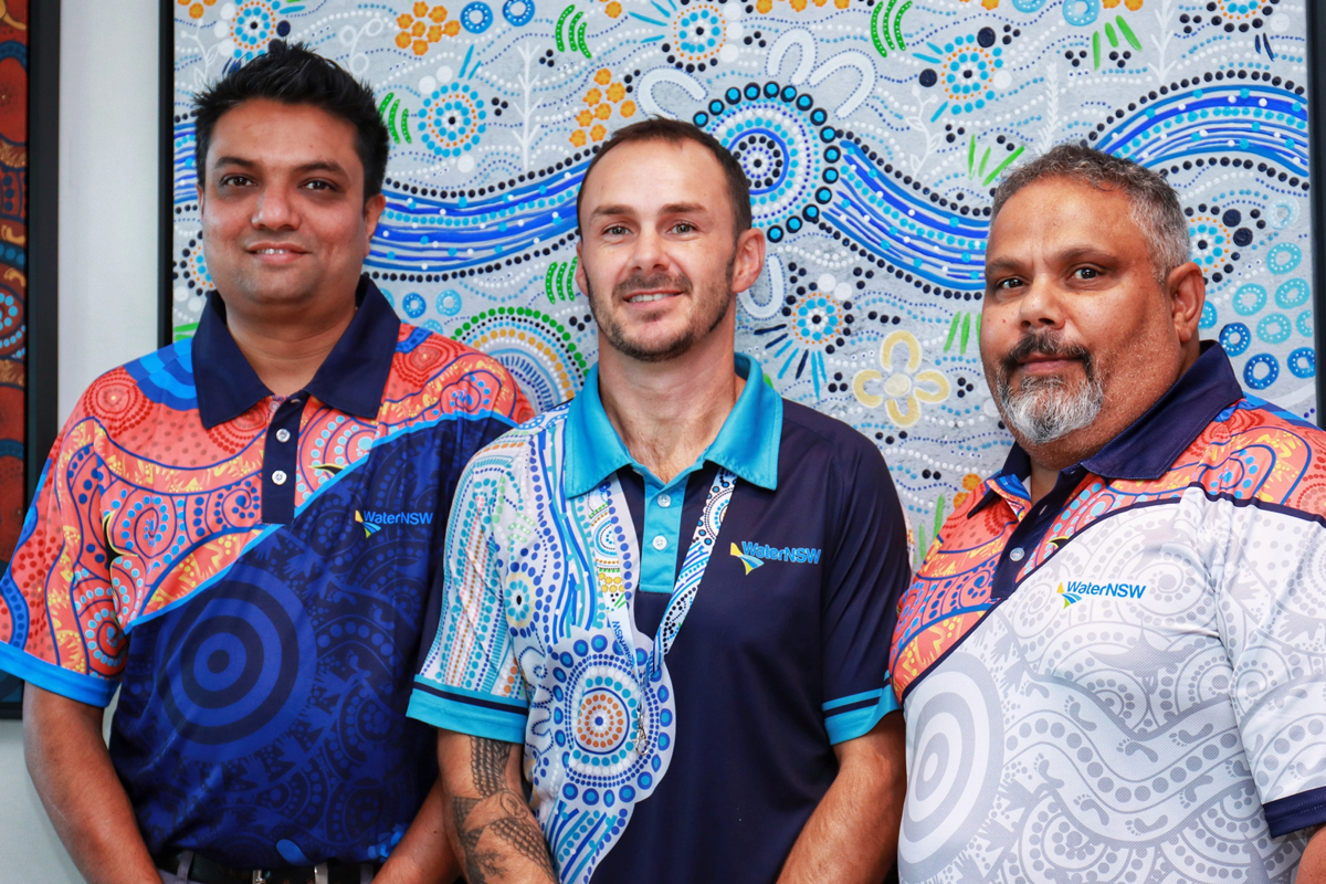 WaterNSW employees Jaymin Raval, Duane Byrnes and Michael Brown, standing in front of our dedicated reconciliation wall at the Parramatta office.  